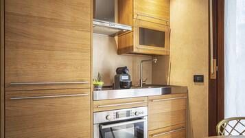 Una cocina compacta con armarios de madera, una cafetera Bosch, un lavabo y un horno.