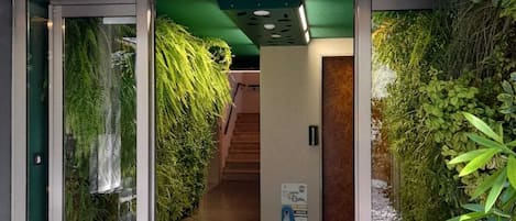 A hotel entrance with a green wall, a circular light fixture, and a welcome mat with the name 'COSTARICA'.