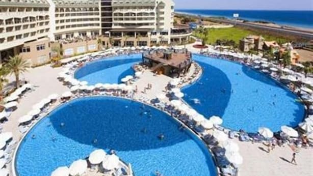 A hotel with multiple swimming pools, a beachfront view, and a large building with balconies.