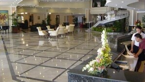 A spacious lobby with a polished tile floor, a reception desk with a floral arrangement, and a staircase leading to an upper level.
