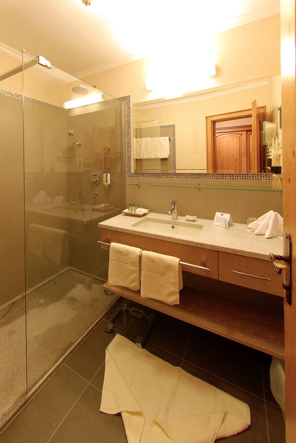 Un baño moderno con ducha envuelta en vidrio, un lavabo con espejo y un mueble de tocador de madera con toallas.