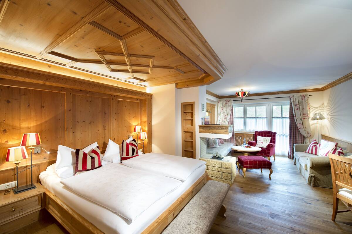 A wooden-paneled bedroom with a large bed, bedside lamps, a bench, a chair, and a sofa.