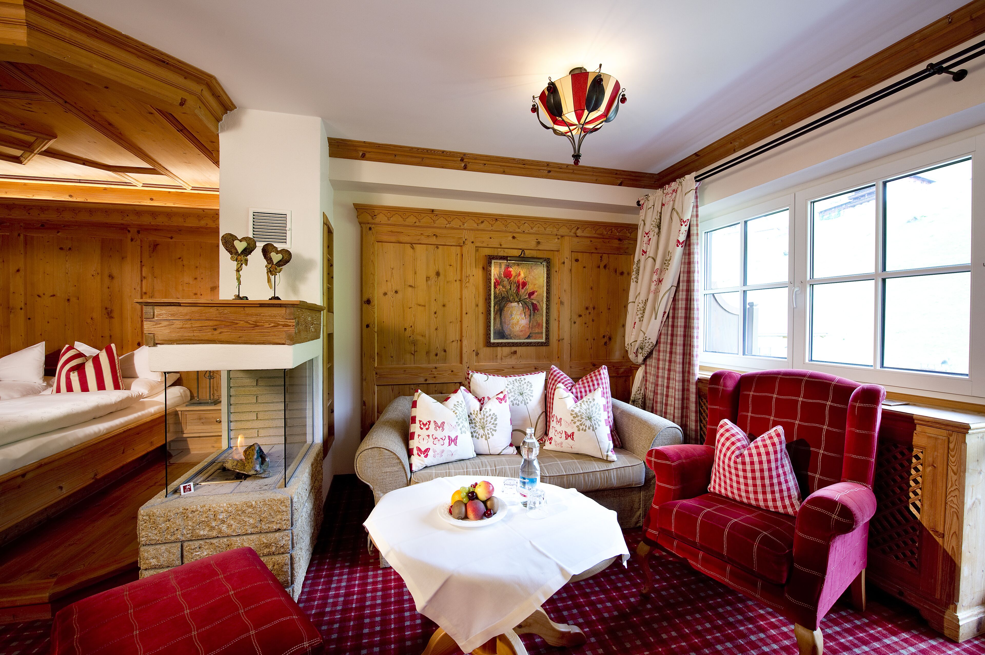 A cozy room with a fireplace, a sofa, a red armchair, and a table with fruit.