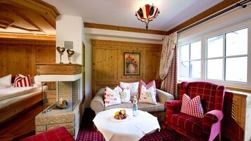 A cozy room with a fireplace, a sofa, a red armchair, and a table with fruit.