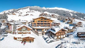 Een bergresort bedekt met sneeuw, met houten gebouwen, skipistes en een helderblauwe lucht.