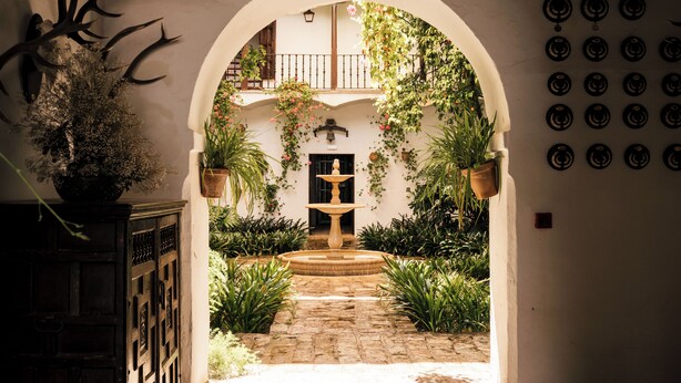 An arched entrance to a courtyard with a fountain, potted plants, and a wall with circular decorations. - Hotel Cortijo el Esparragal (Gerena)