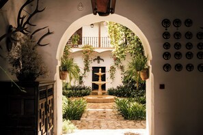 Una entrada arqueada a un patio con una fuente, plantas en macetas y una pared con adornos circulares.