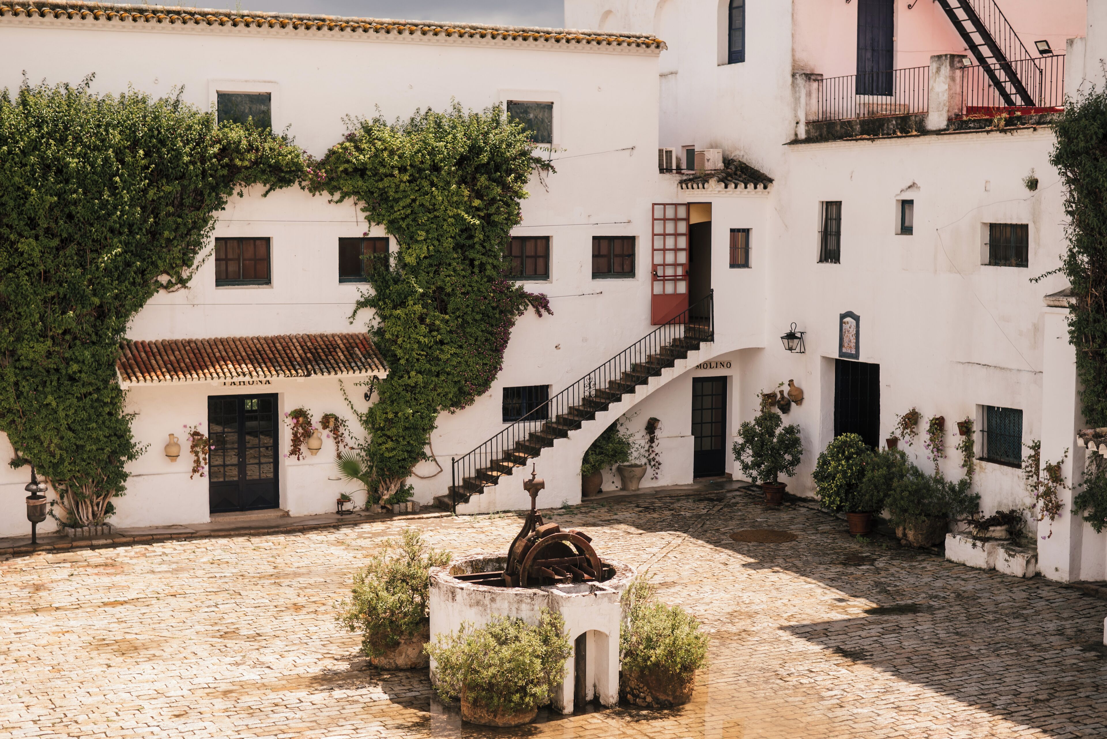 Un patio con suelo de adoquines, una fuente central y edificios blancos con balcones y ventanas.