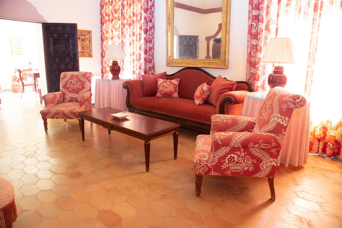 Un salon avec un canapé rouge, des fauteuils assortis, une table basse en bois et des rideaux à motifs.