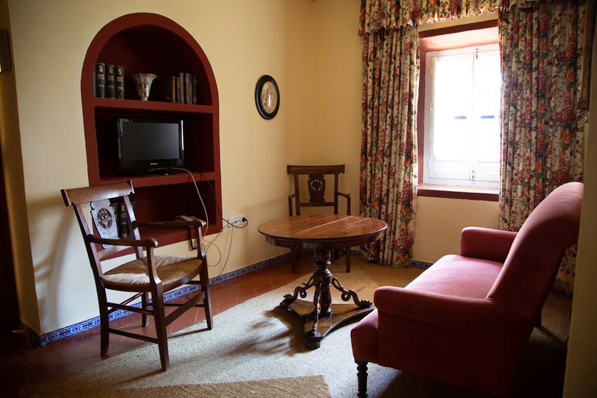 Un salon avec une bibliothèque en bois, un téléviseur, une table ronde et un fauteuil rouge.