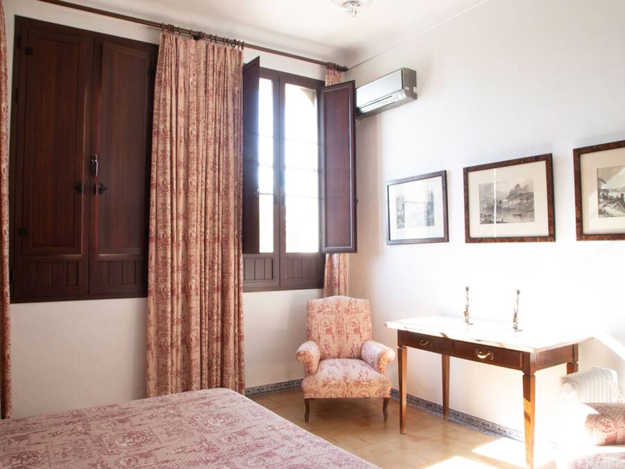 A bedroom with a bed, a chair, a desk, and a window with curtains.