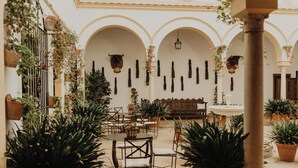 An outdoor patio area with tables and chairs, potted plants, and hanging planters. - Hotel Cortijo el Esparragal (Gerena)