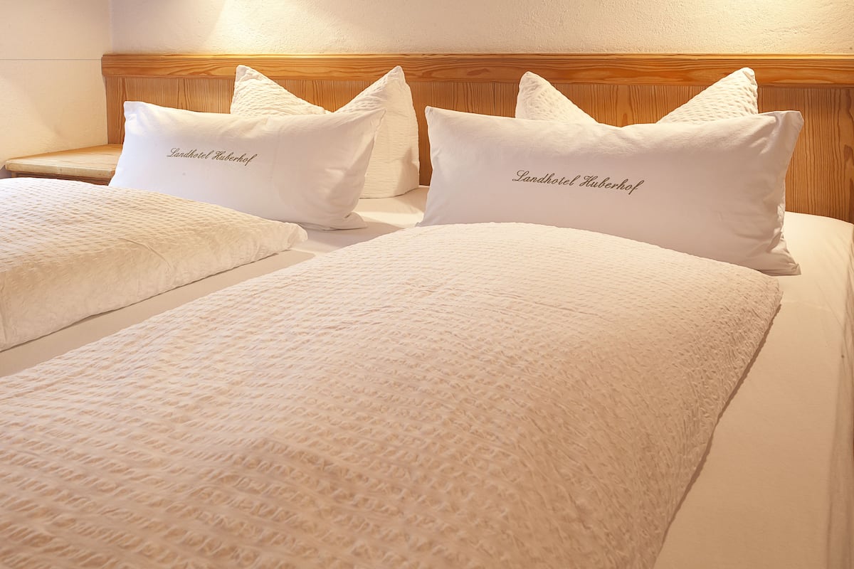 Een hotelkamer met een houten hoofdbord, twee bedden met witte beddengoed en kussens met de naam van het hotel geborduurd.