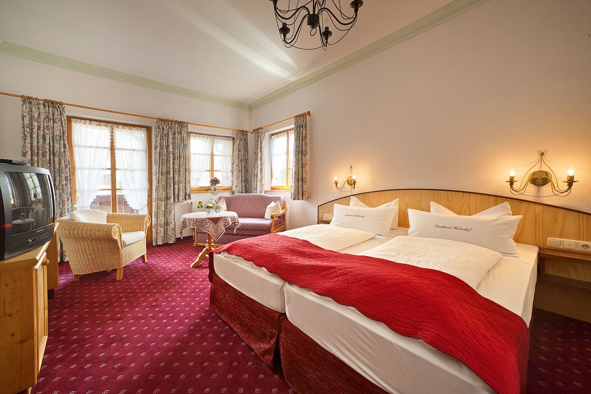 Een hotelkamer met een groot bed, een televisie, een tafeltje met een vaas, en een stoel.