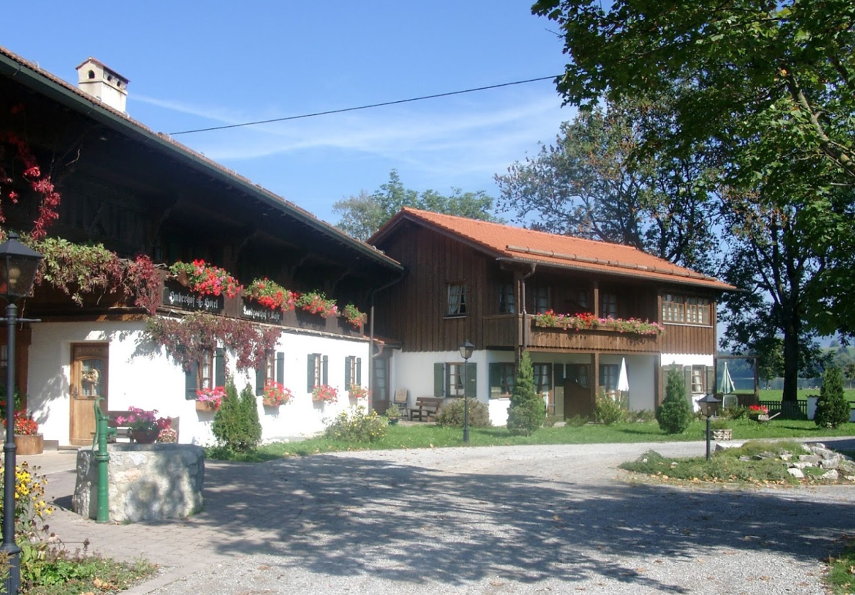 A traditional chalet with a sloped roof, wooden balconies with flower boxes, and a gravel driveway.