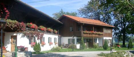A traditional chalet with a sloped roof, wooden balconies with flower boxes, and a gravel driveway.