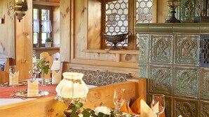 Een eetruimte met een tafel gedekt voor twee personen, met een wit tafelkleed, oranje servetringen en een decoratieve lamp.