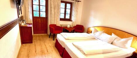 A hotel room with a bed, two chairs, a small table, a TV, and a window with curtains.