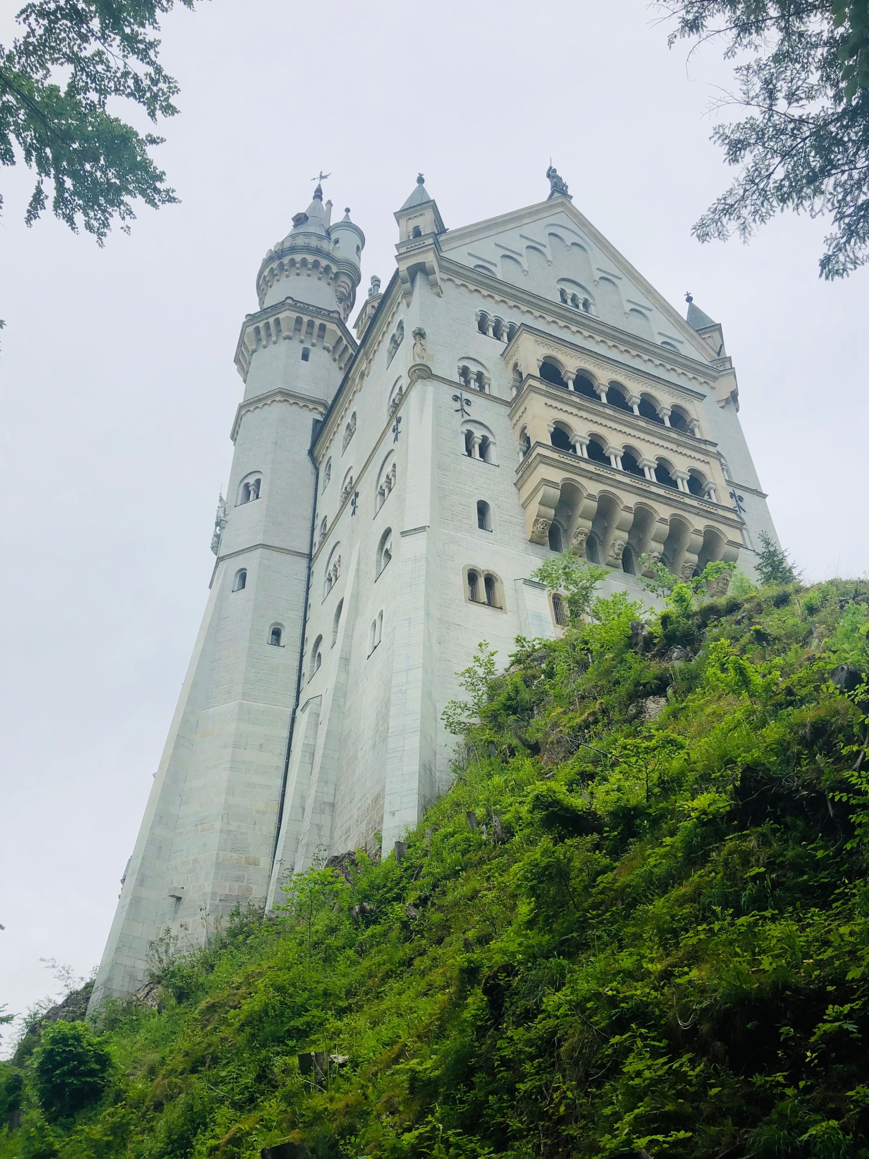 A large, historic building with multiple towers and a prominent clock tower, surrounded by lush greenery.