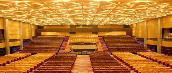 A large auditorium with tiered seating and a geometric ceiling design. - Gokulam Park Hotel & Convention Centre (Kanayannur)