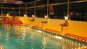 An indoor swimming pool with steps leading into the water, surrounded by walls with built-in lighting fixtures.