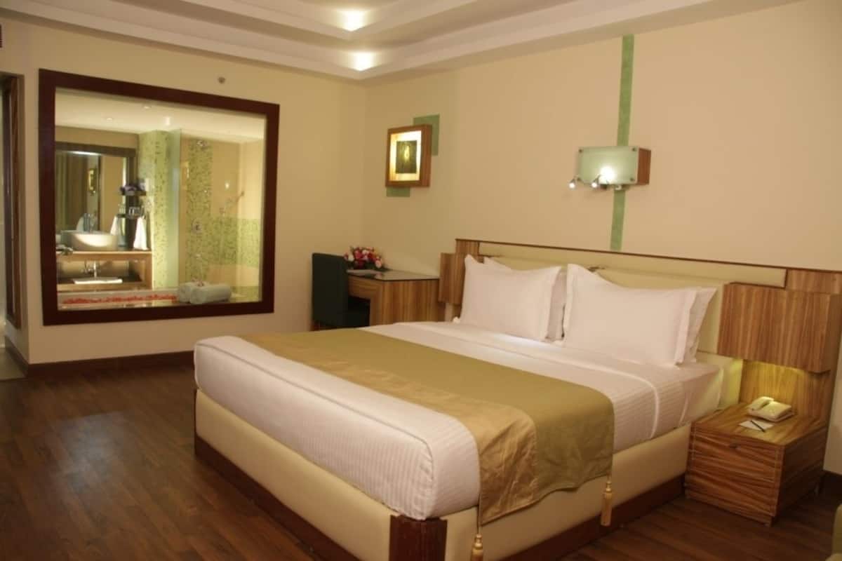 A hotel room with a large bed, a bedside table, a nightstand, a mirror, and a wall-mounted light fixture.