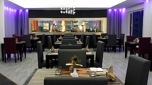 A modern restaurant with a central bar, multiple dining tables, and chairs arranged for guests.