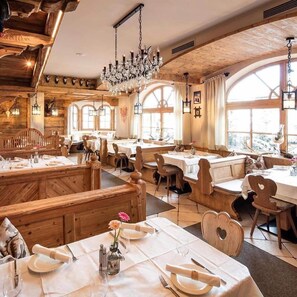 A restaurant with wooden interiors, multiple dining tables, and a chandelier.