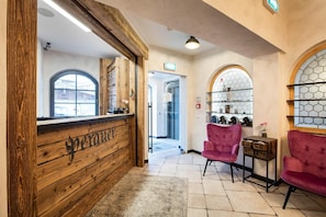 A reception area with a wooden reception desk, a pink chair, and a tiled floor.