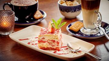 A dessert plate with a layered cake, a cup of coffee, and a bowl of cookies on a wooden table.