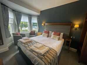 A hotel room with a large bed, two bedside tables, a chair, and a window with curtains.