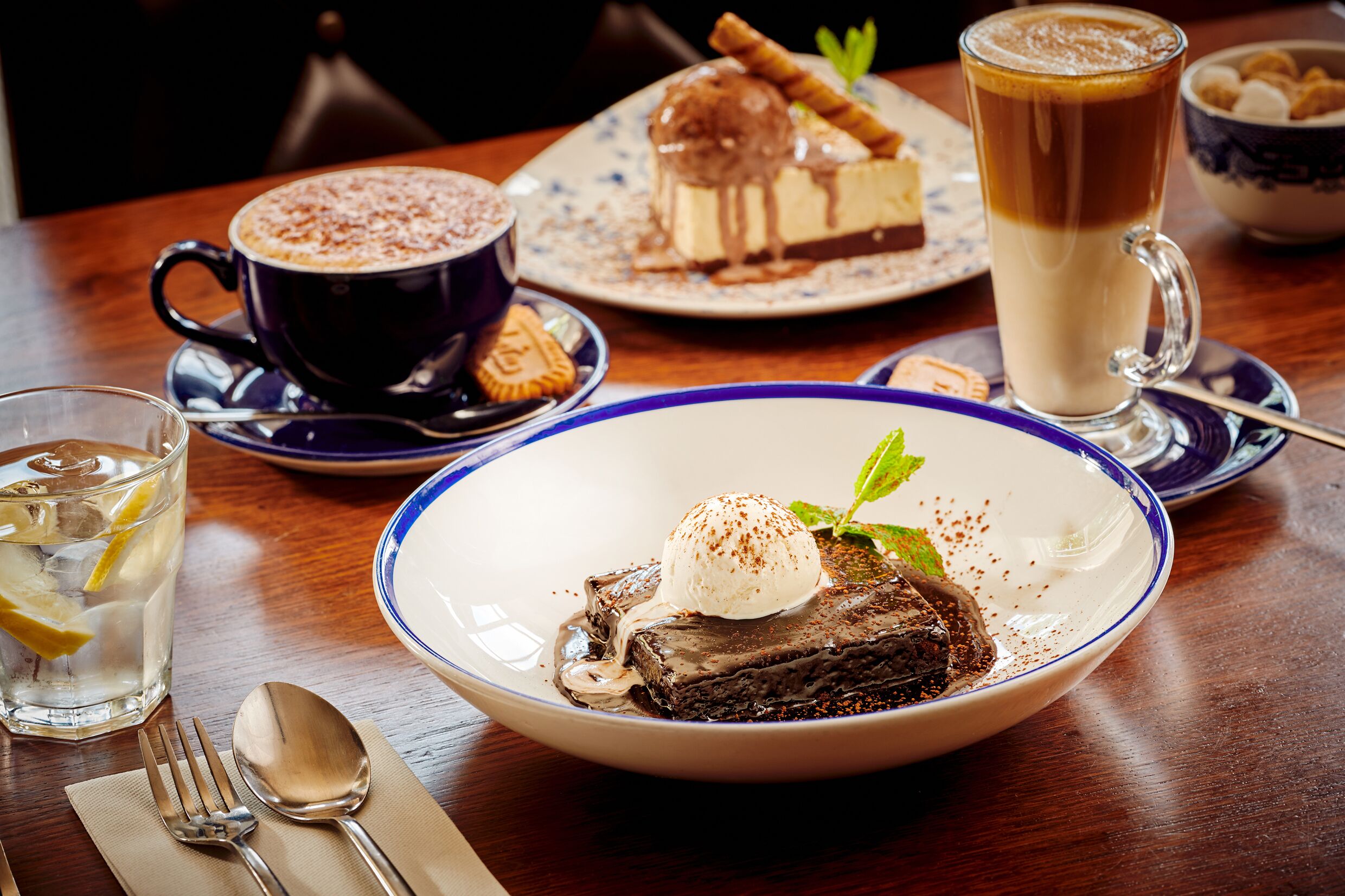 Ein Dessertteller mit Schokoladendessert und einer Kugel Eis, eine Tasse Kaffee und ein Glas Eistee auf einem Holztisch.