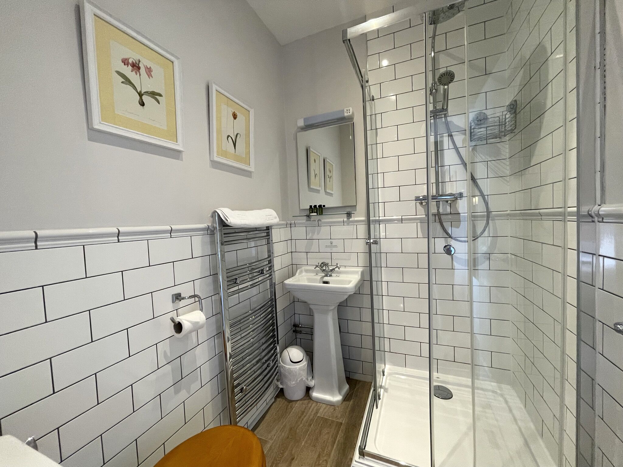 A bathroom with white tiled walls, a sink, a toilet, and a shower area.