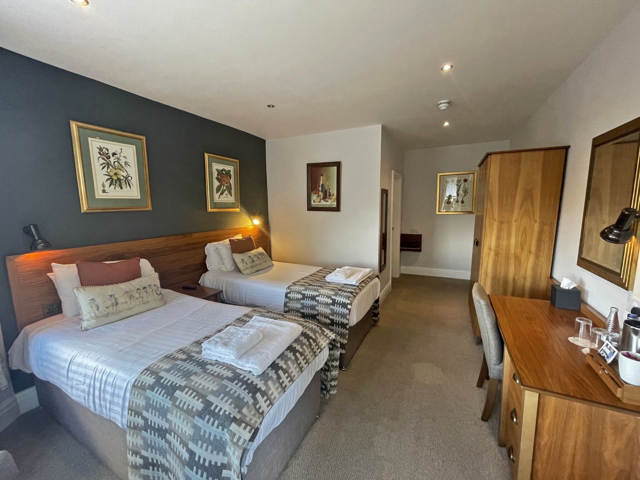 A hotel room with two beds, a wooden dresser, and framed artwork on the walls.
