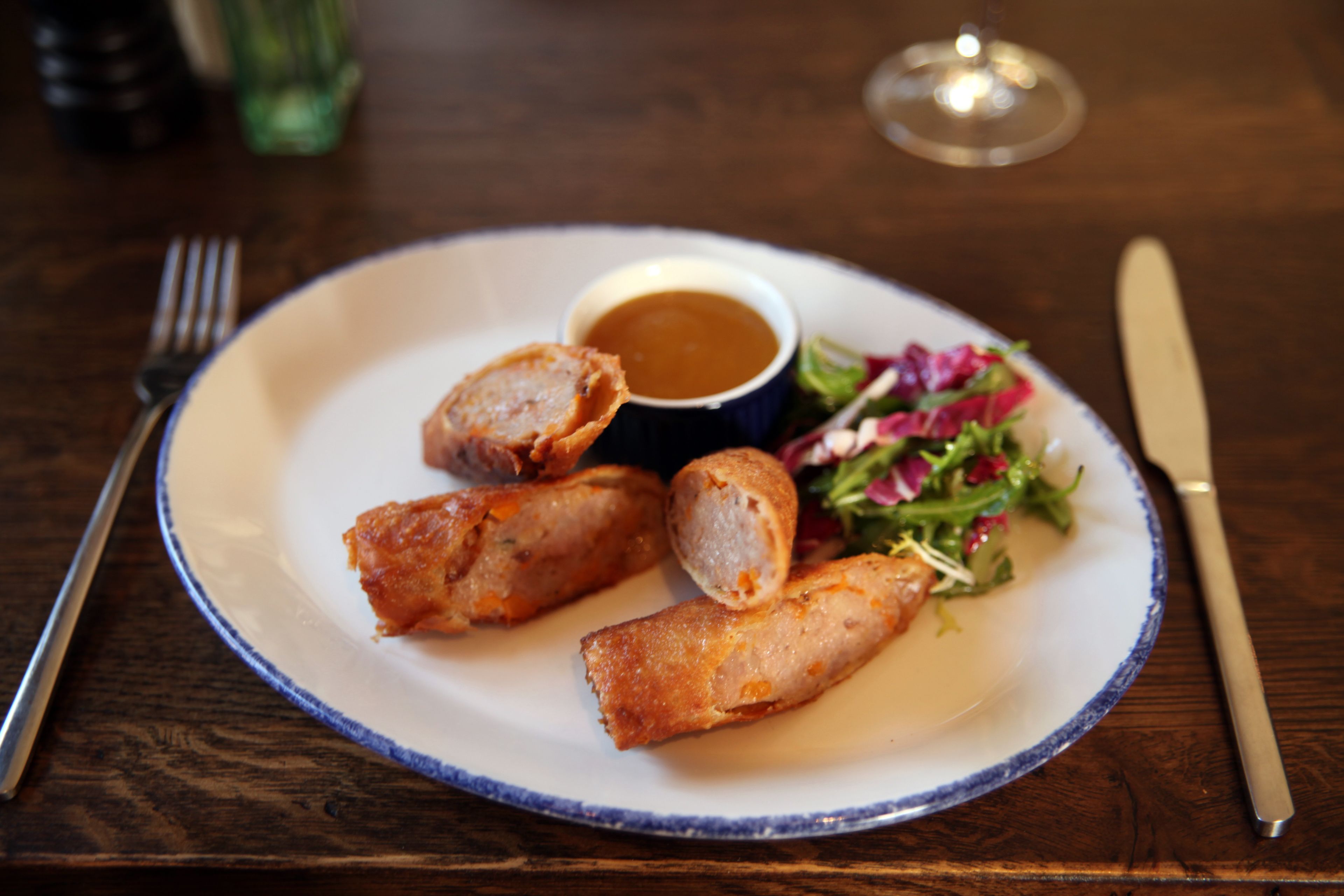 A plate with food, a fork, and a knife on a wooden table.
