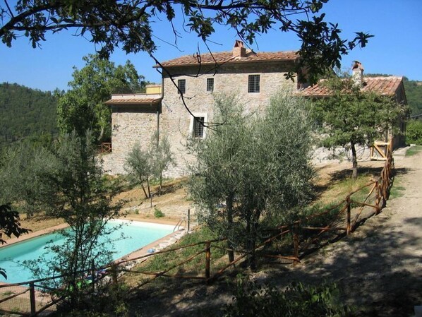 A stone building with a swimming pool, surrounded by trees and hills.