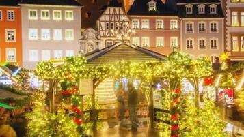A traditional European market scene with a central stall decorated with Christmas lights and greenery.