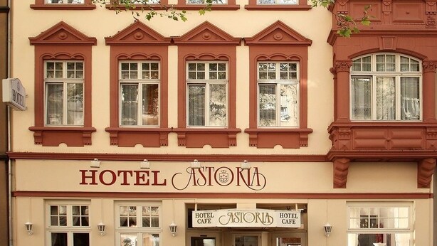 A hotel with a classic facade, featuring a central entrance with double doors, a cafe, and a sign indicating the presence of a hotel and cafe. - Astoria Hotel Trier (Trier)