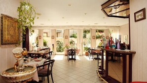 A spacious dining area with multiple tables and chairs, a decorative fountain, and a large mirror. - Astoria Hotel Trier (Trier)