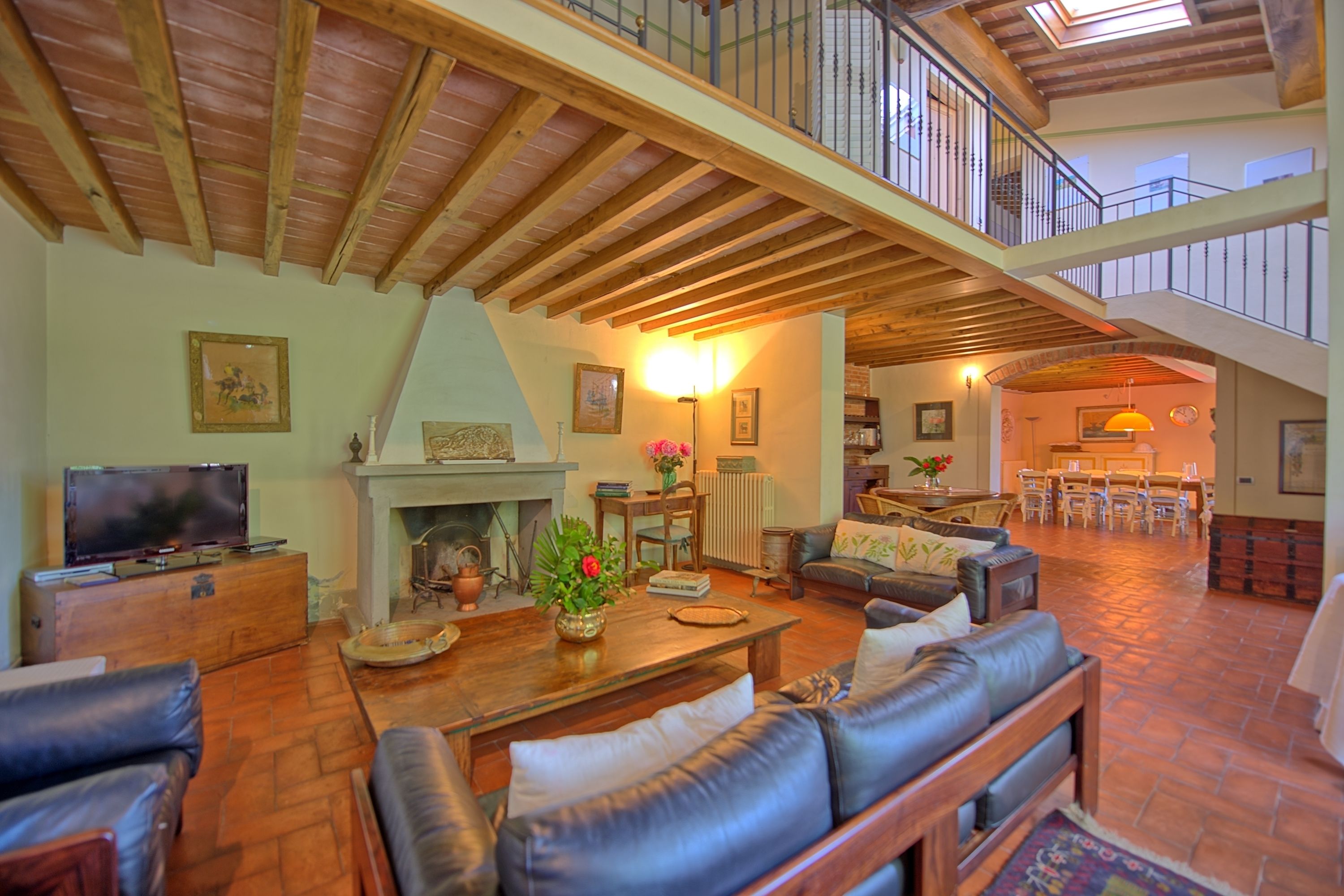 A spacious living room with a fireplace, leather sofas, a television, and a dining area with chairs and a table.