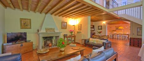 A spacious living room with a fireplace, leather sofas, a television, and a dining area with chairs and a table.