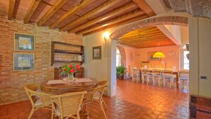 A rustic dining area with a brick wall, wooden ceiling beams, and a brick archway leading to another room. - Villa Fontine (Castelfranco di Sotto)
