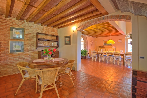 A rustic dining area with a brick wall, wooden ceiling beams, and a brick archway leading to another room.