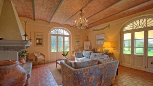 A spacious living room with a patterned sofa, a chandelier, and large windows. - Villa Fontine (Castelfranco di Sotto)