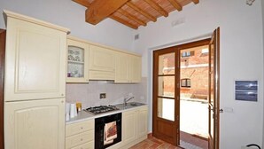A compact kitchen with white cabinets, a gas stove, and a sink. There's a door leading to a patio with a view of a brick building. - Pienza (Pienza)