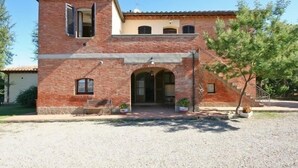A two-story brick building with a central arched entrance, a small upper balcony, and a gravel driveway. - Pienza (Pienza)