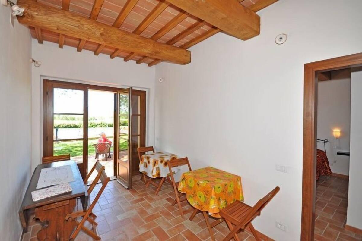A dining area with a wooden table and chairs, a window with a view of the outdoors, and a door leading to another room.