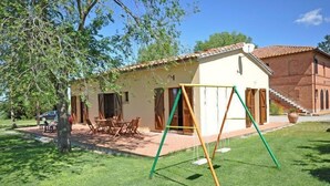 A house with a patio, a swing set, and a brick building in the background. - Pienza (Pienza)