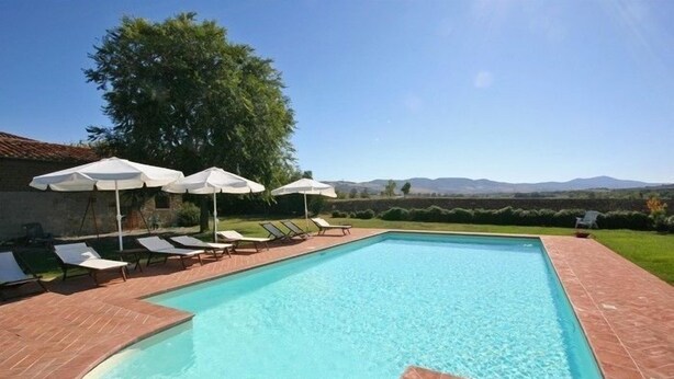 A rectangular swimming pool with a tiled edge, surrounded by lounge chairs and white umbrellas. - Pienza (Pienza)