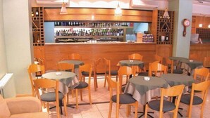 A restaurant with multiple tables and chairs, a bar area with shelves of bottles, and a clock on the wall. - Alcor Hotel (Mendoza)